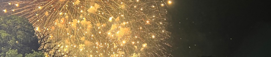 A little boy looking at a starbust of New Year's Eve fireworks.