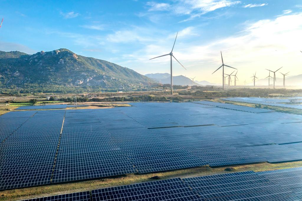 Picture showing a field of solar panels in the foreground and wind turbines in the background. 