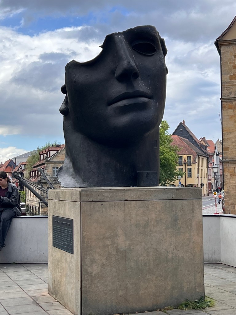 Metal sculpture of a human head with parts of its skull missing.